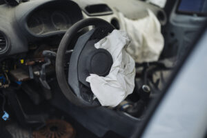 Deployed driver-side airbag hanging from steering wheel inside an abandoned car interior, illustrating airbag deployment and post-deployment state