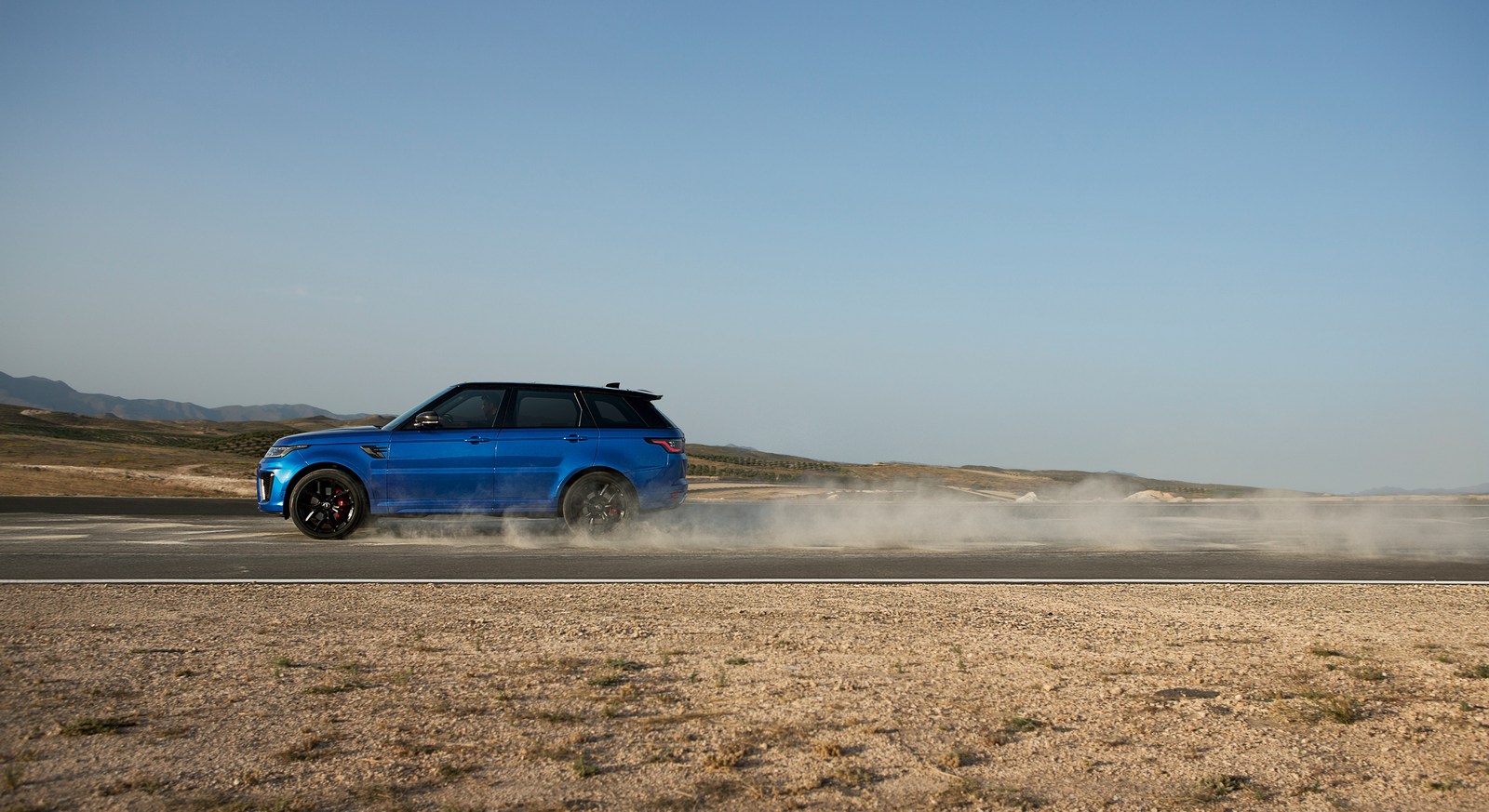 Range Rover Sport L494 side profile on a desert road kicking up dust, showing 22-inch wheels and the long bonnet line