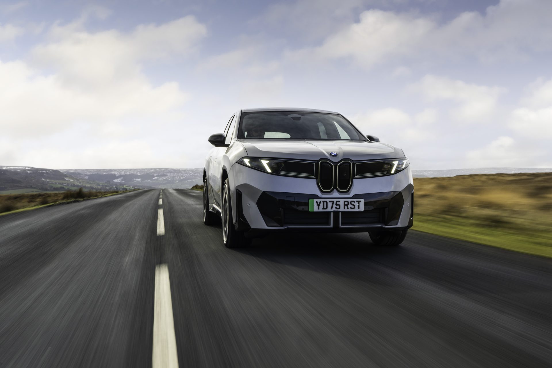 New BMW iX3 electric SUV driving on a UK moorland road, front view with UK number plate