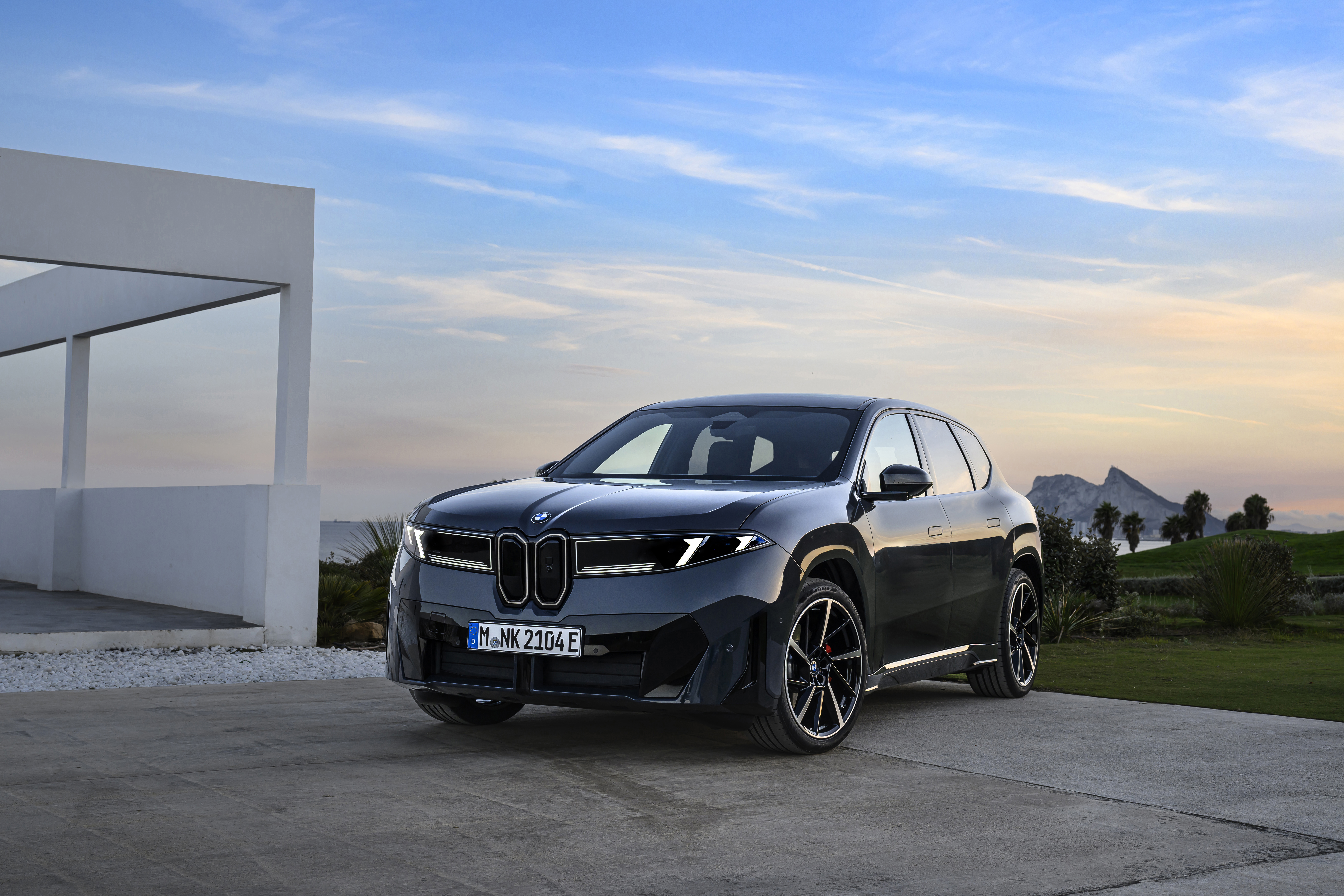 BMW iX3 Neue Klasse front three-quarter view at dusk, white architecture behind