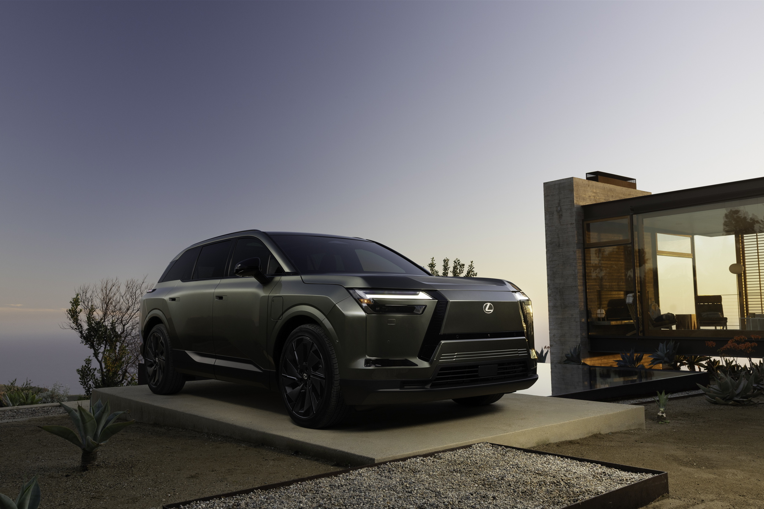 Lexus TZ electric SUV front three-quarter view outside a modern house at dusk