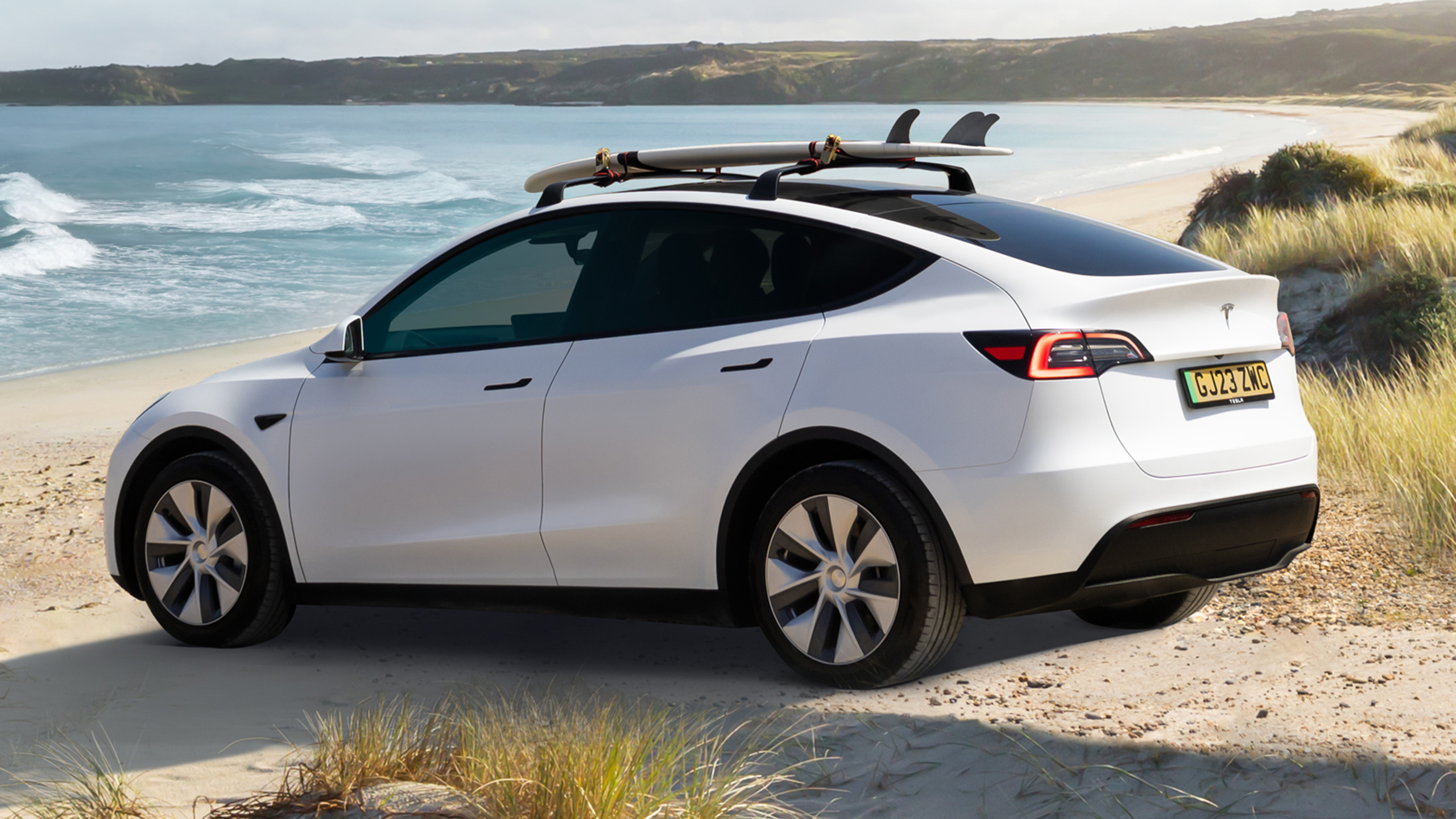 Used Tesla Model Y in white on a UK plate parked by a beach with roof bars