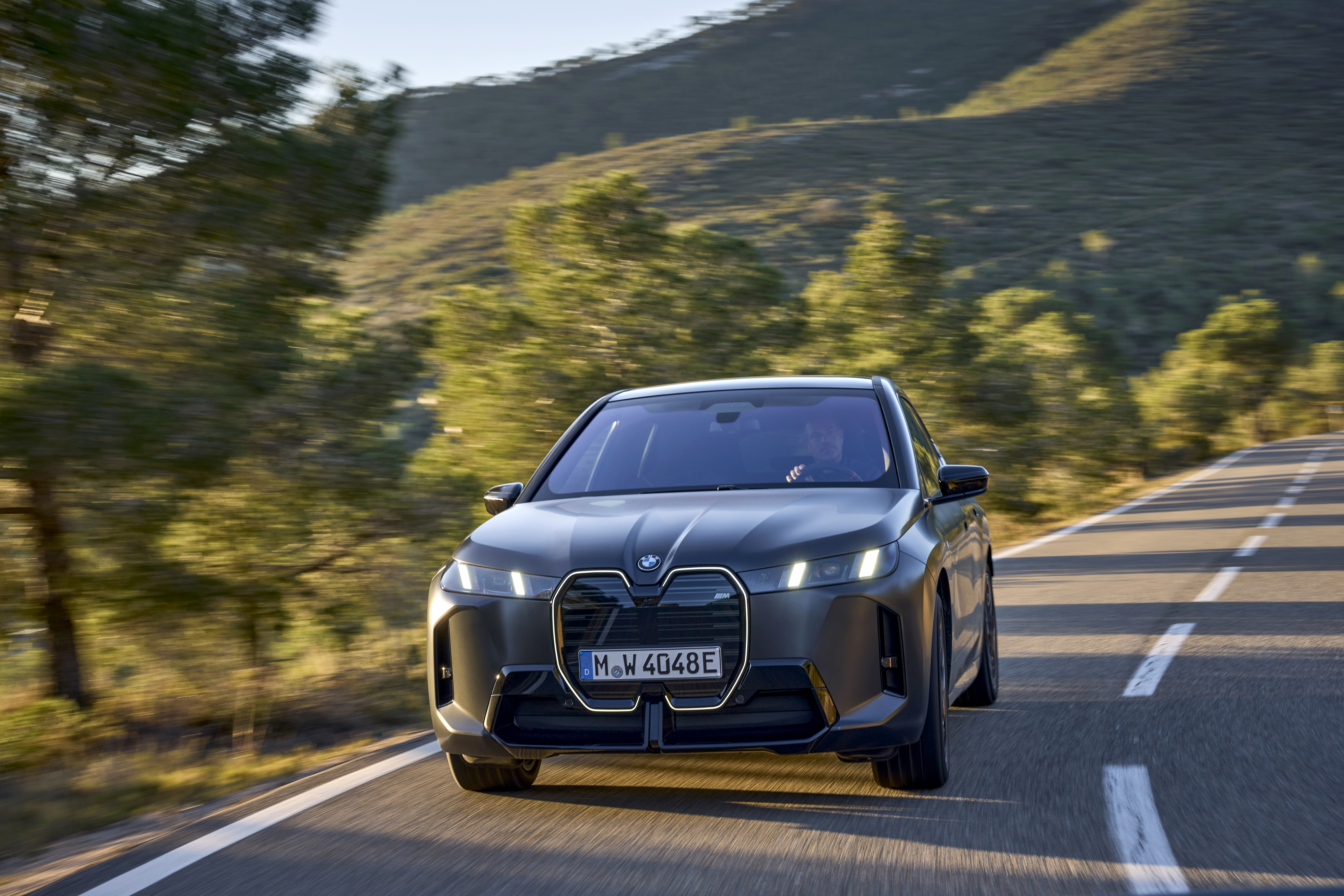 BMW iX electric SUV head-on on a tree-lined road