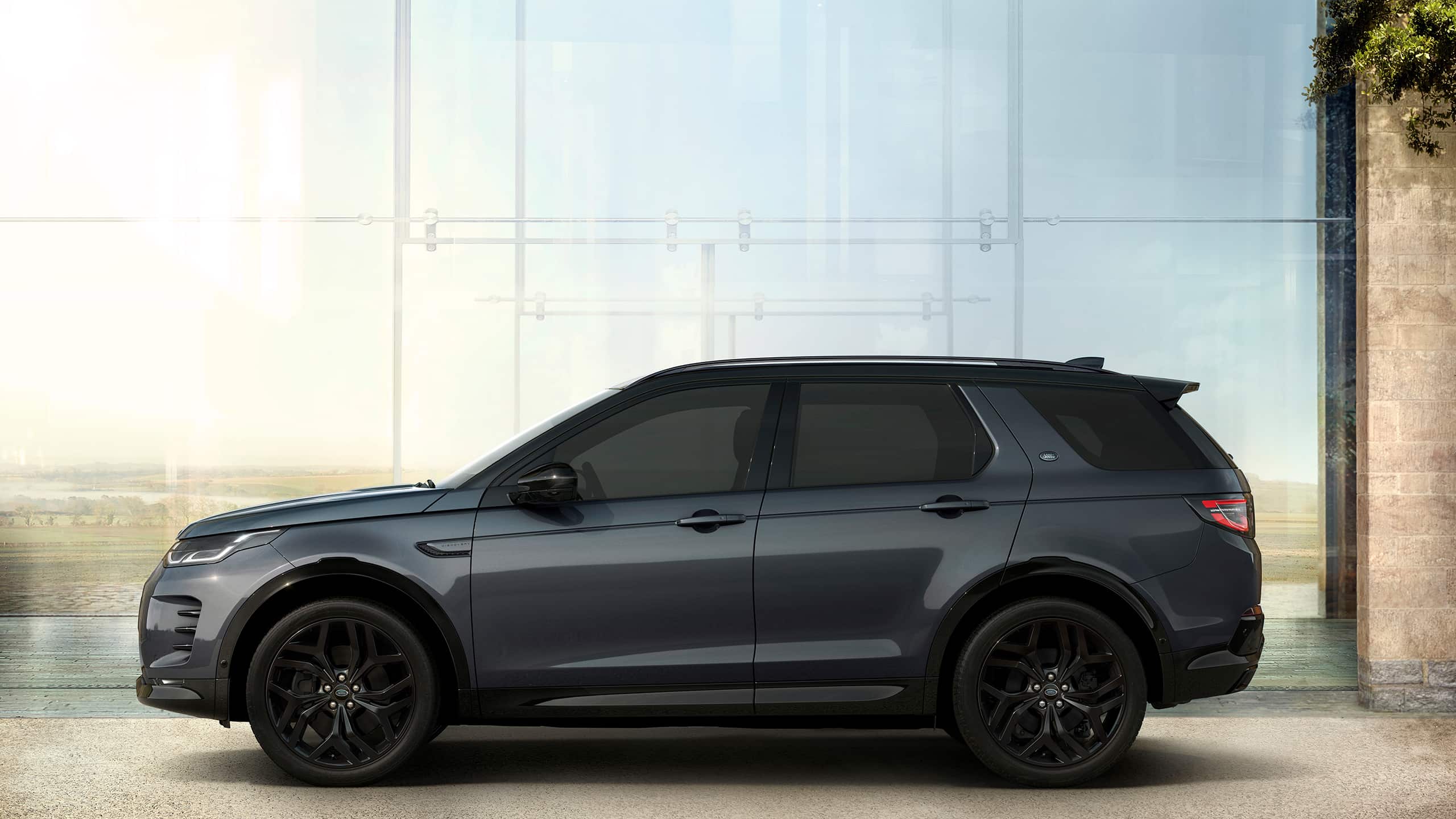 Grey Land Rover Discovery Sport in side profile outside a glass building